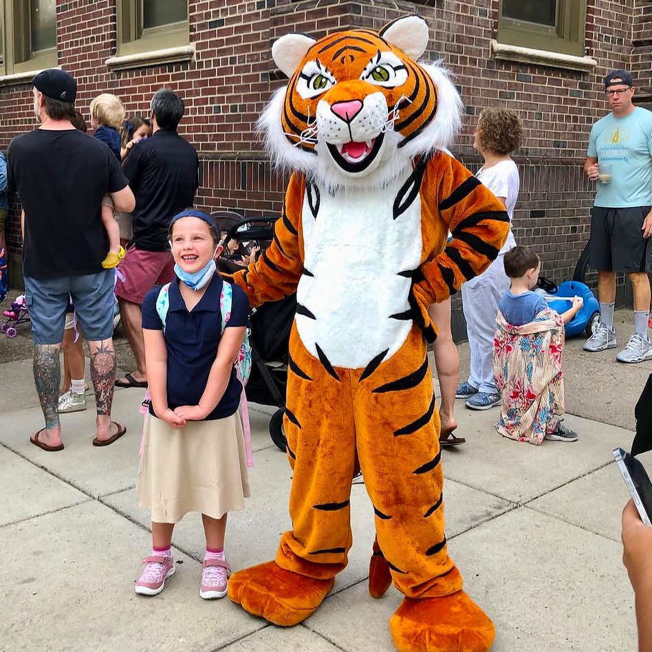 A student poses with the Bache-Martin tiger mascot during a school community event outside the school building.